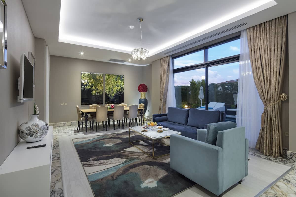 A modern living room with a blue sofa, a coffee table, and a dining area with a chandelier.
