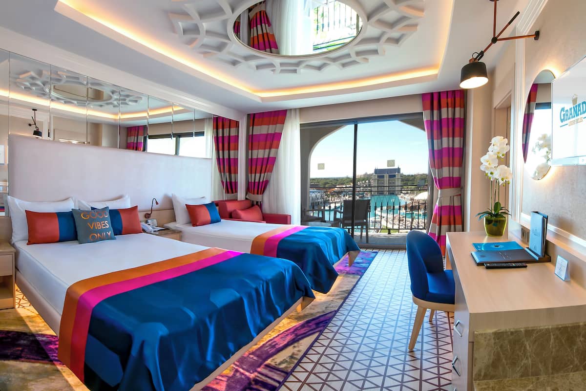 A hotel room with two beds, a desk, and a view of the city.