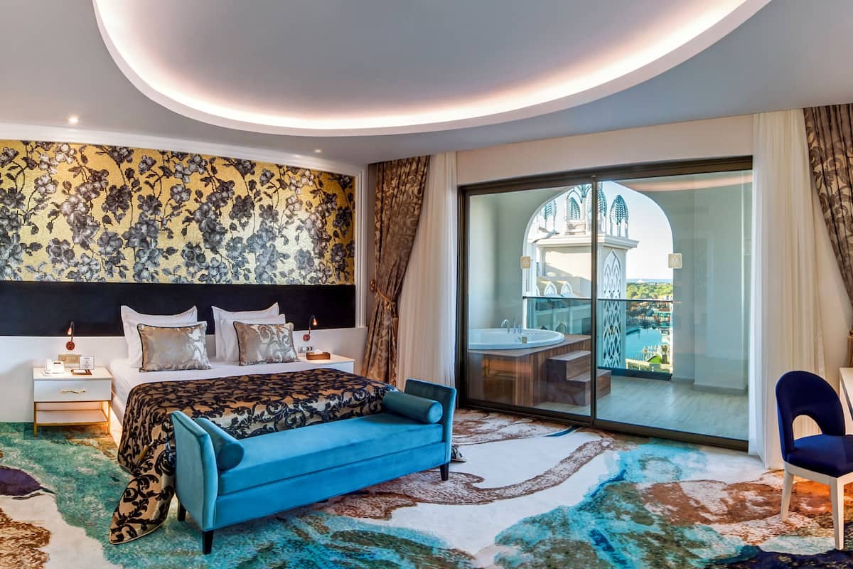 A modern hotel room with a large bed, a desk, and a view of a pool and building.