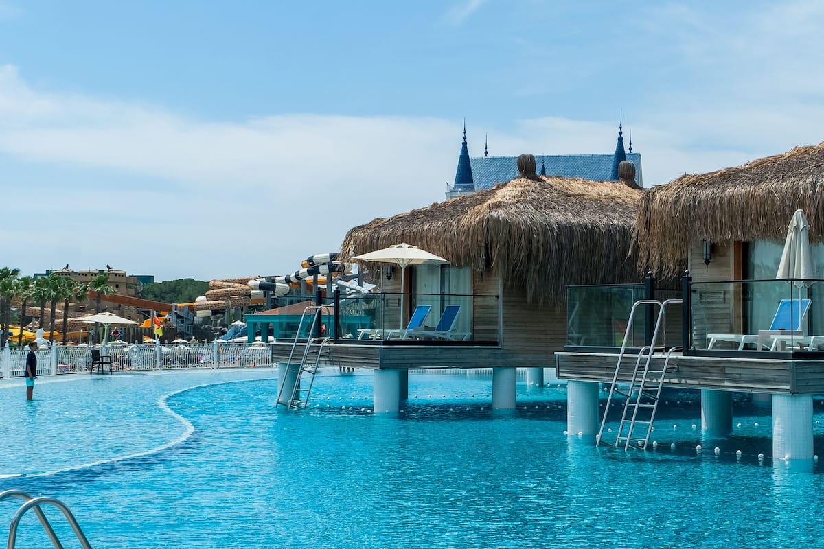 A swimming pool with thatched-roof structures, lounge chairs, and a clear sky.
