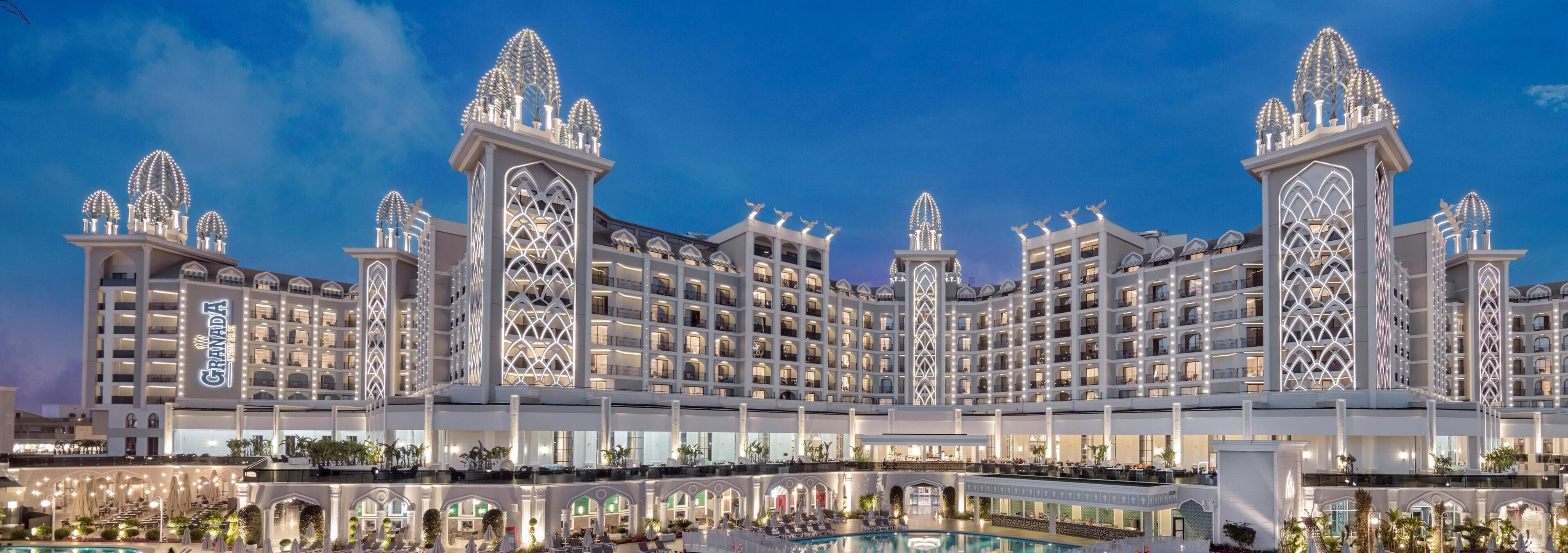 Un hotel grande de varios pisos con fachada simétrica, múltiples balcones y un patio central con piscina.