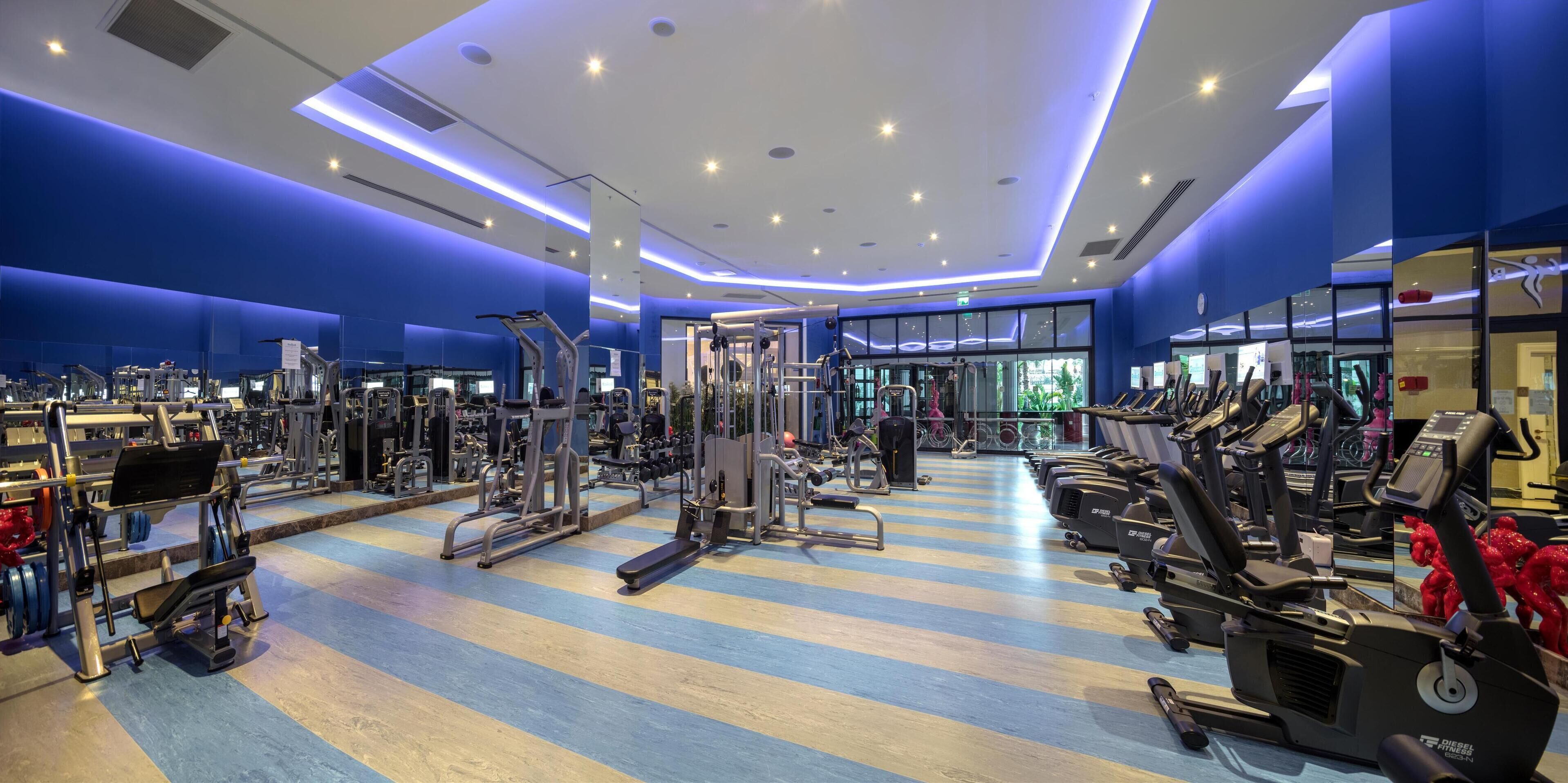 A gym with various exercise equipment, a blue and white striped floor, and a large mirror reflecting the equipment.