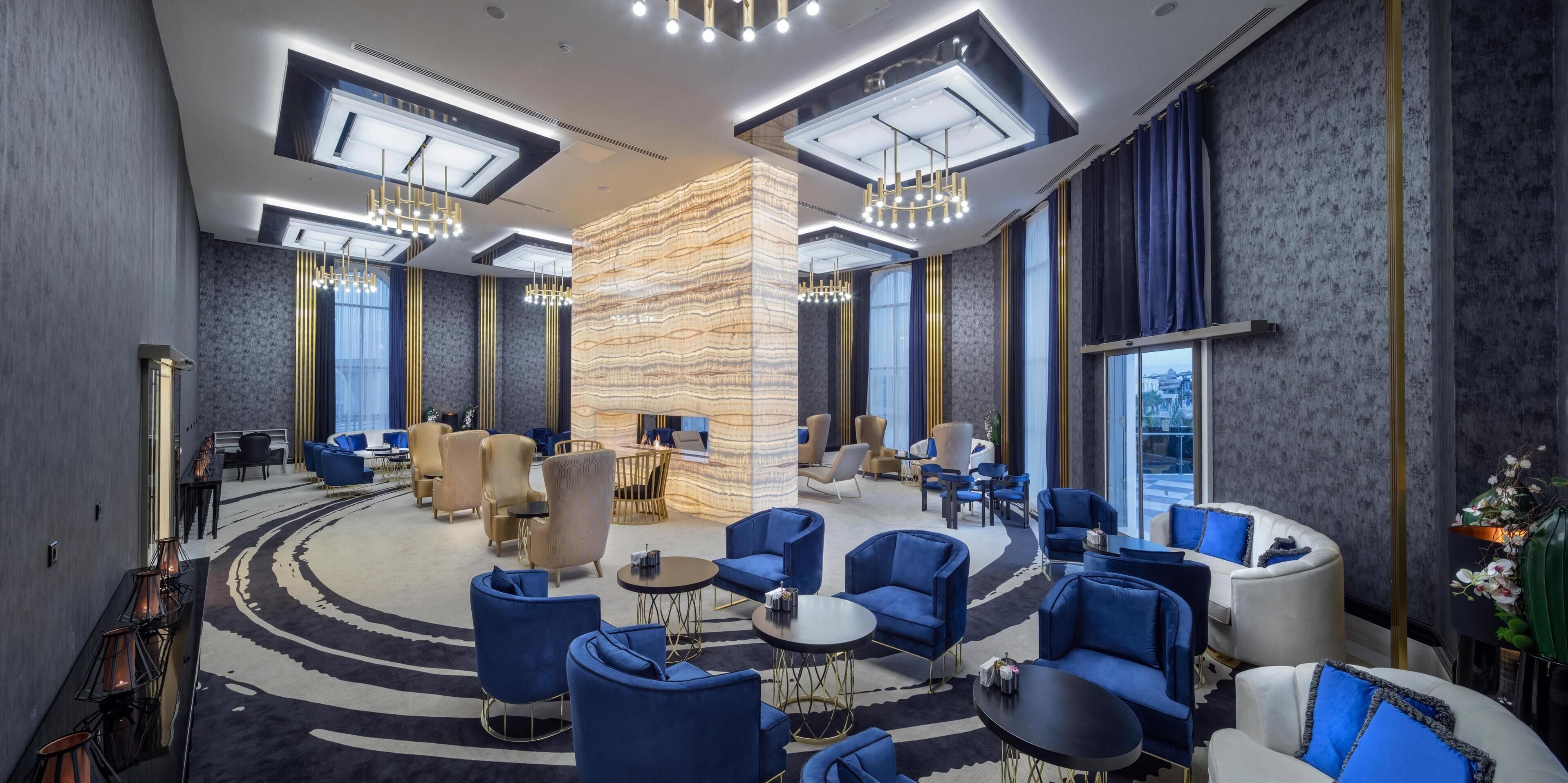 Un moderno vestíbulo de hotel con una zona de estar central, ventanas amplias e iluminación contemporánea.