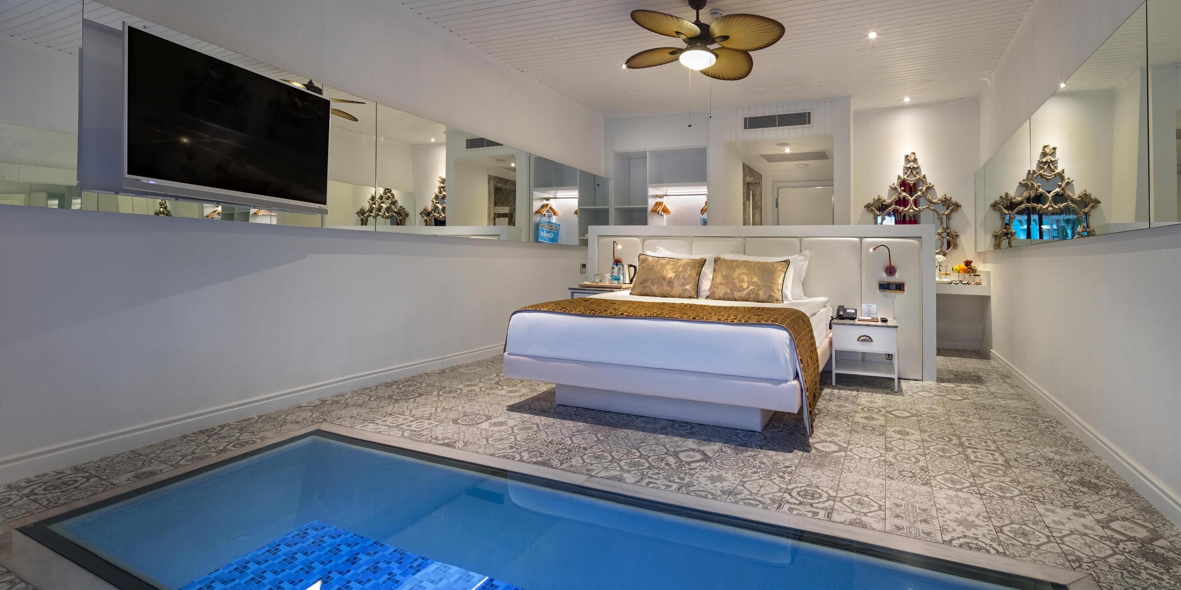 Ein modernes Schlafzimmer mit einem großen Bett, integriertem Fernseher, Deckenventilator und einem kleinen Nachttisch mit Lampe.