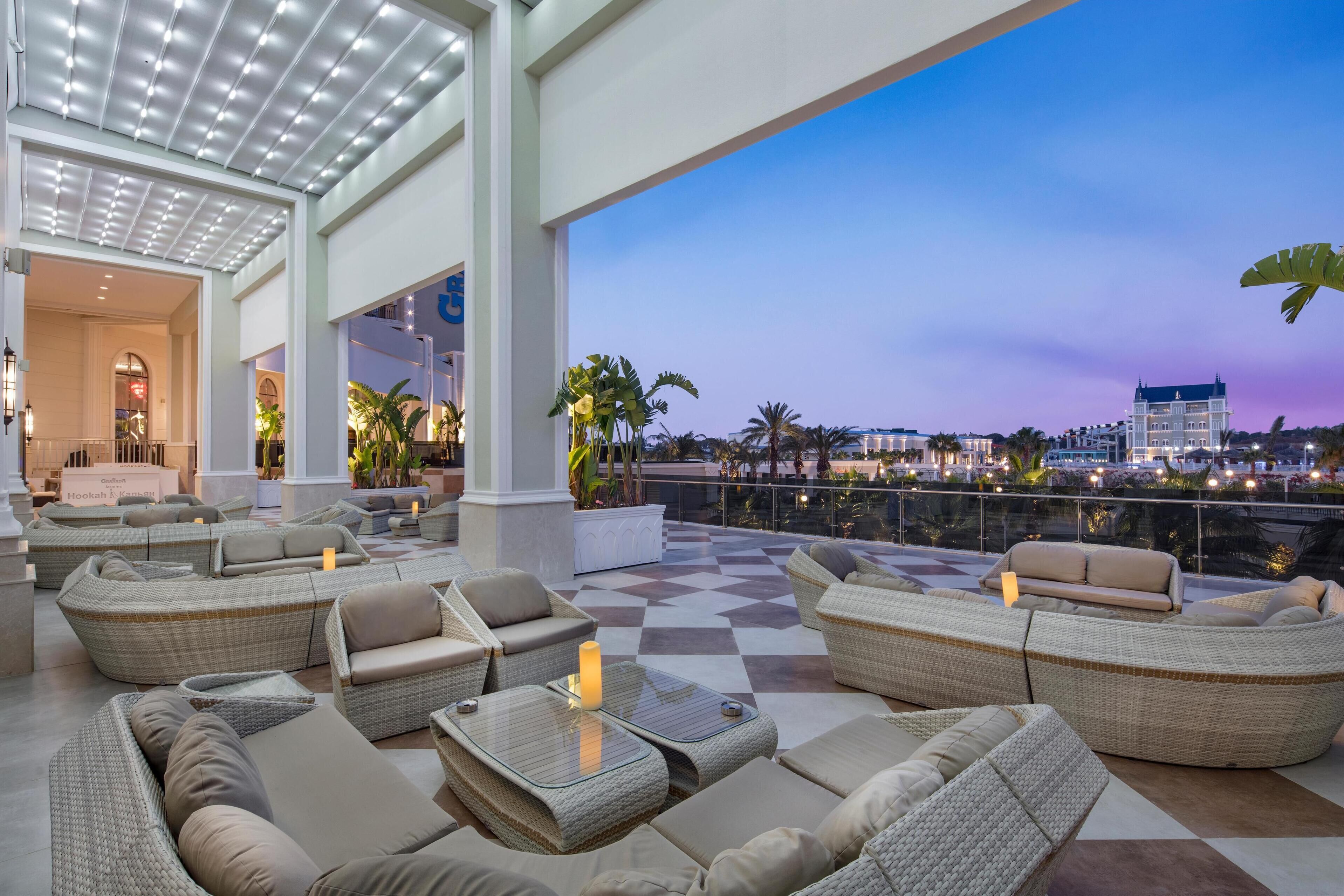 A rooftop lounge with wicker furniture and a view of the cityscape at dusk.