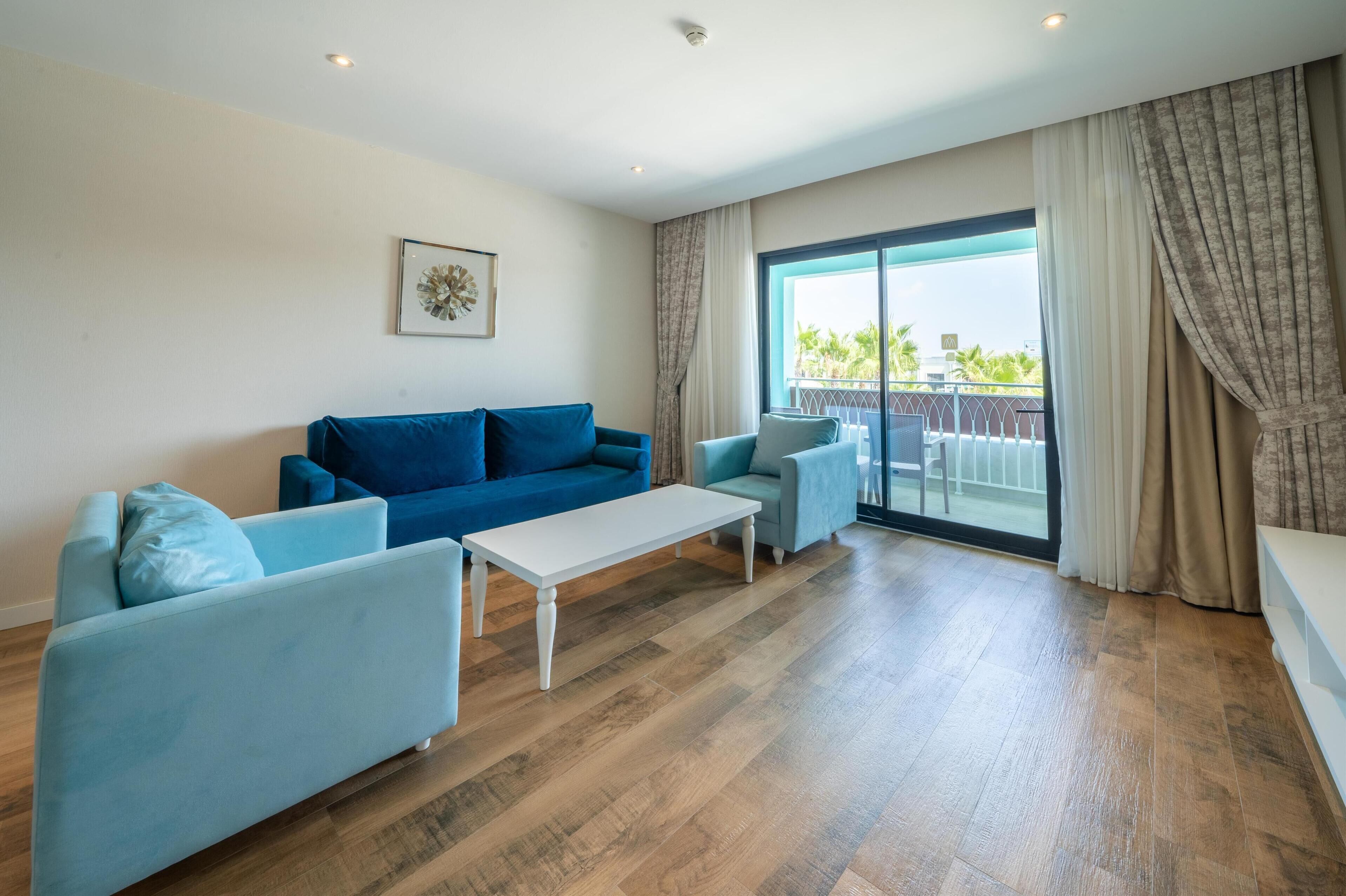 Un salon moderne avec un canapé bleu, une table basse blanche et une vue sur un balcon aménagé avec du mobilier d’extérieur.