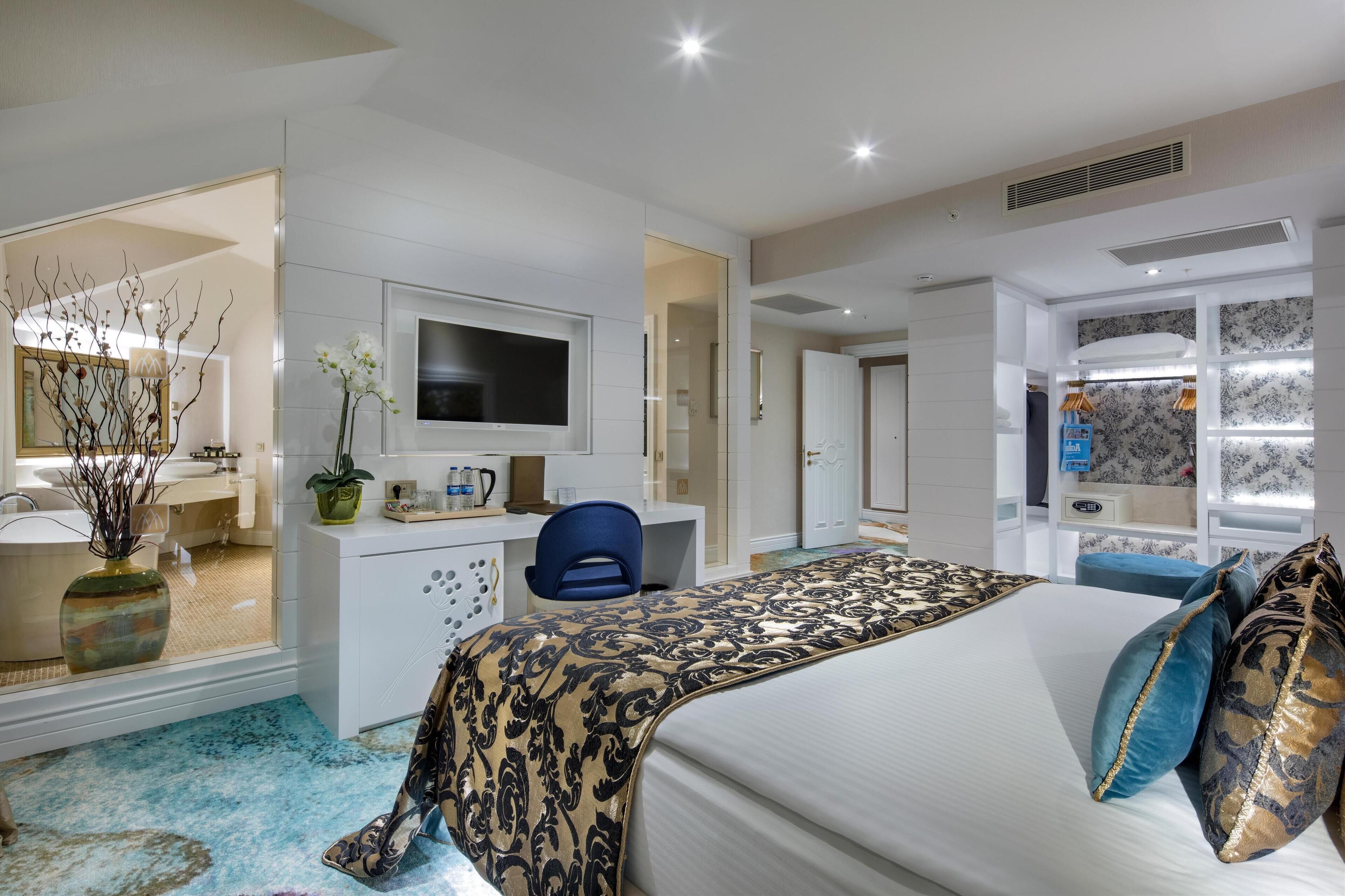 Habitación de hotel moderna con una cama grande, un escritorio con una silla, televisión y un baño visible a través de una puerta abierta.