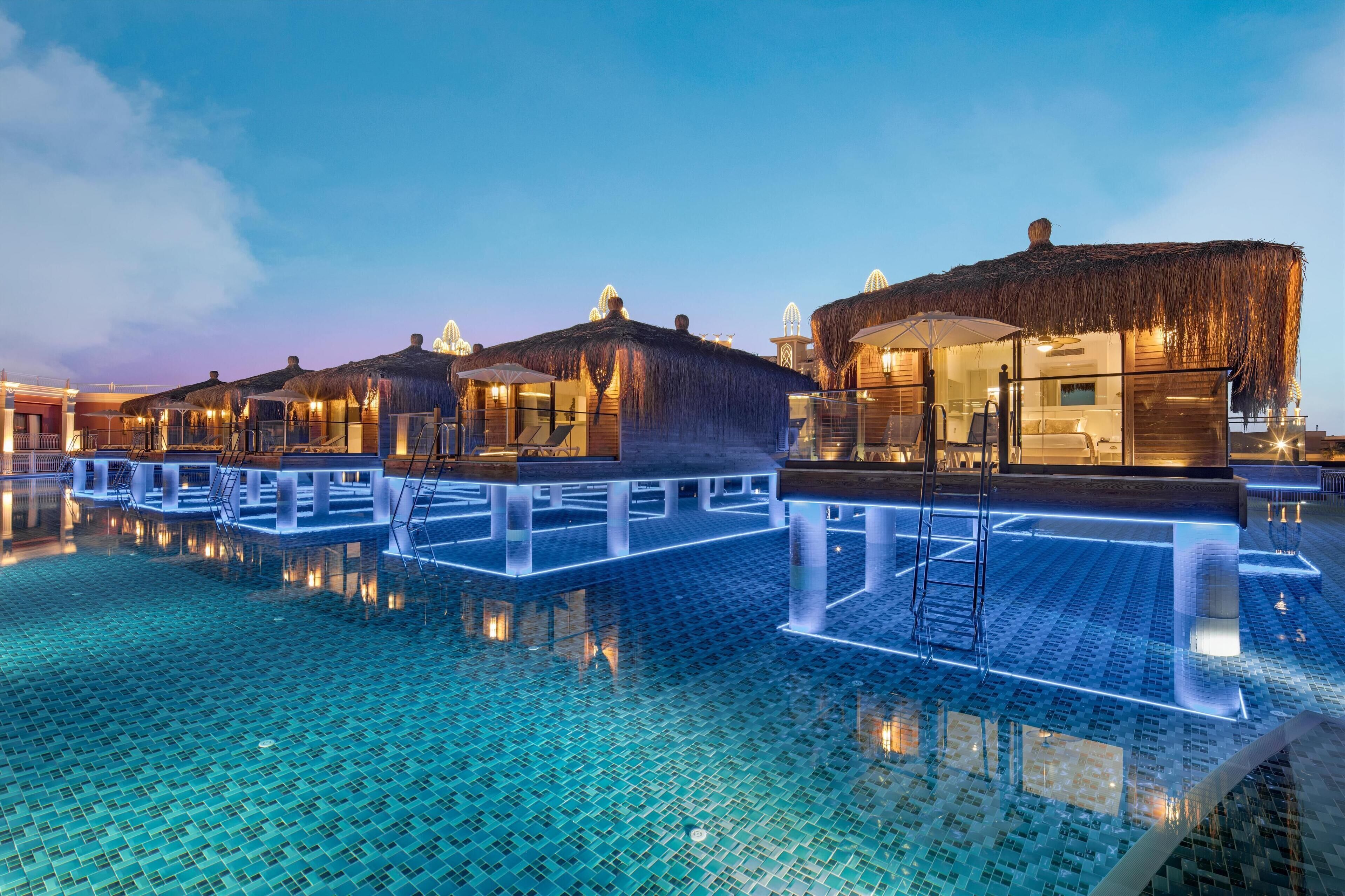 A resort with overwater bungalows, a swimming pool, and a thatched-roof structure.
