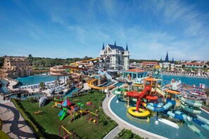 Ein Wasserpark mit verschiedenen Rutschen und Pools, ein schlossartiges Gebäude und eine große Menschenmenge.