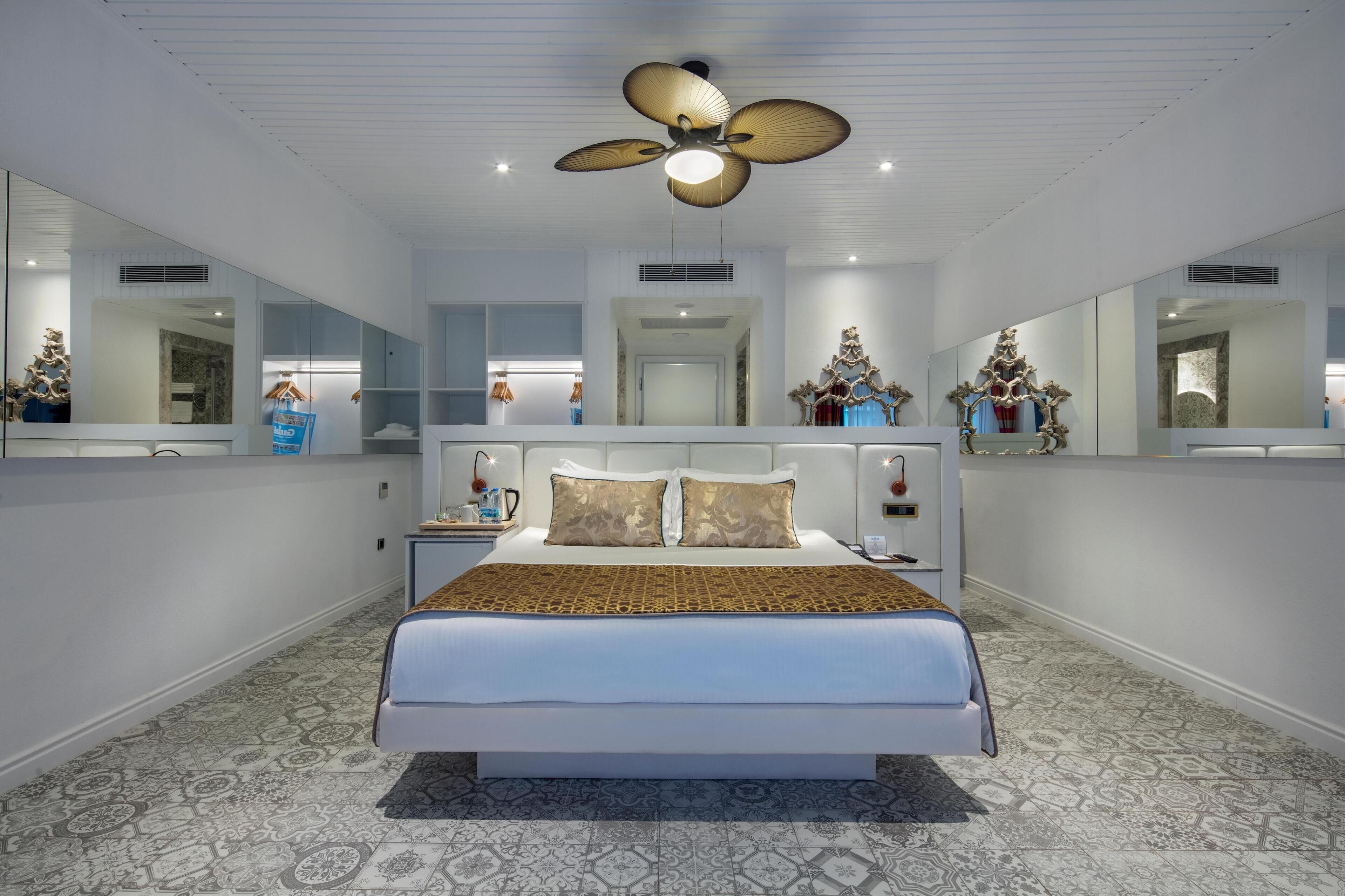 A modern bedroom with a large bed, a ceiling fan, and mirrored walls.
