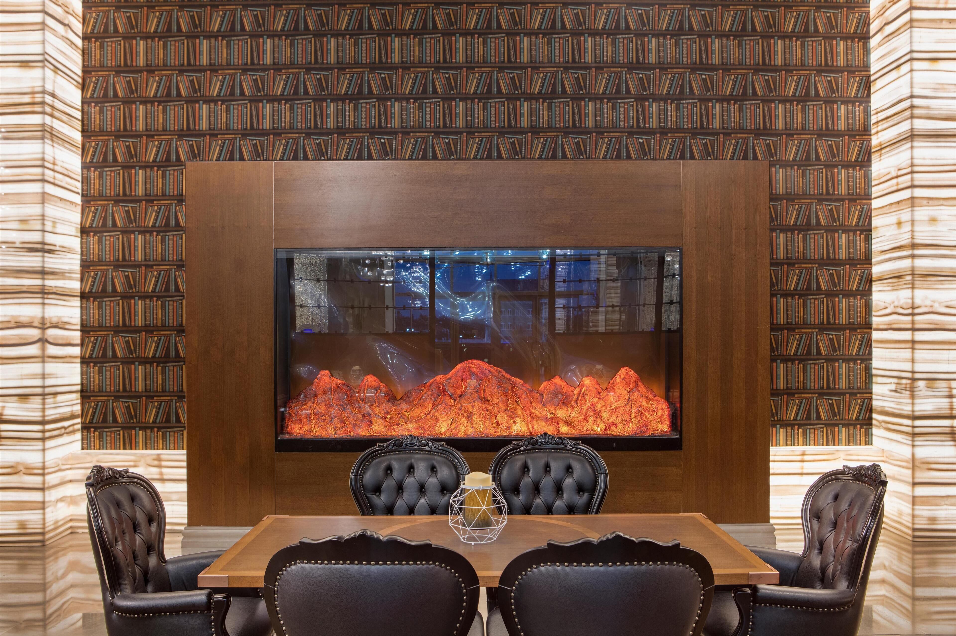 A dining area with a large table, four chairs, a fireplace, and bookshelves.
