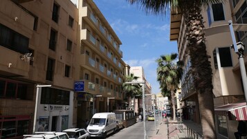 Hotel Rusadir en una calle de la ciudad, con una camioneta blanca estacionada frente, palmeras bordeando la acera y otros edificios al fondo.