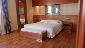 A modern bedroom with a wooden bed frame, a large mirror, and a nightstand with a lamp. - Hotel Rusadir (Melilla)