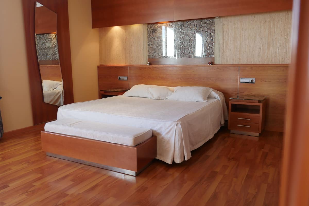 A modern bedroom with a wooden bed frame, a large mirror, and a nightstand with a lamp.