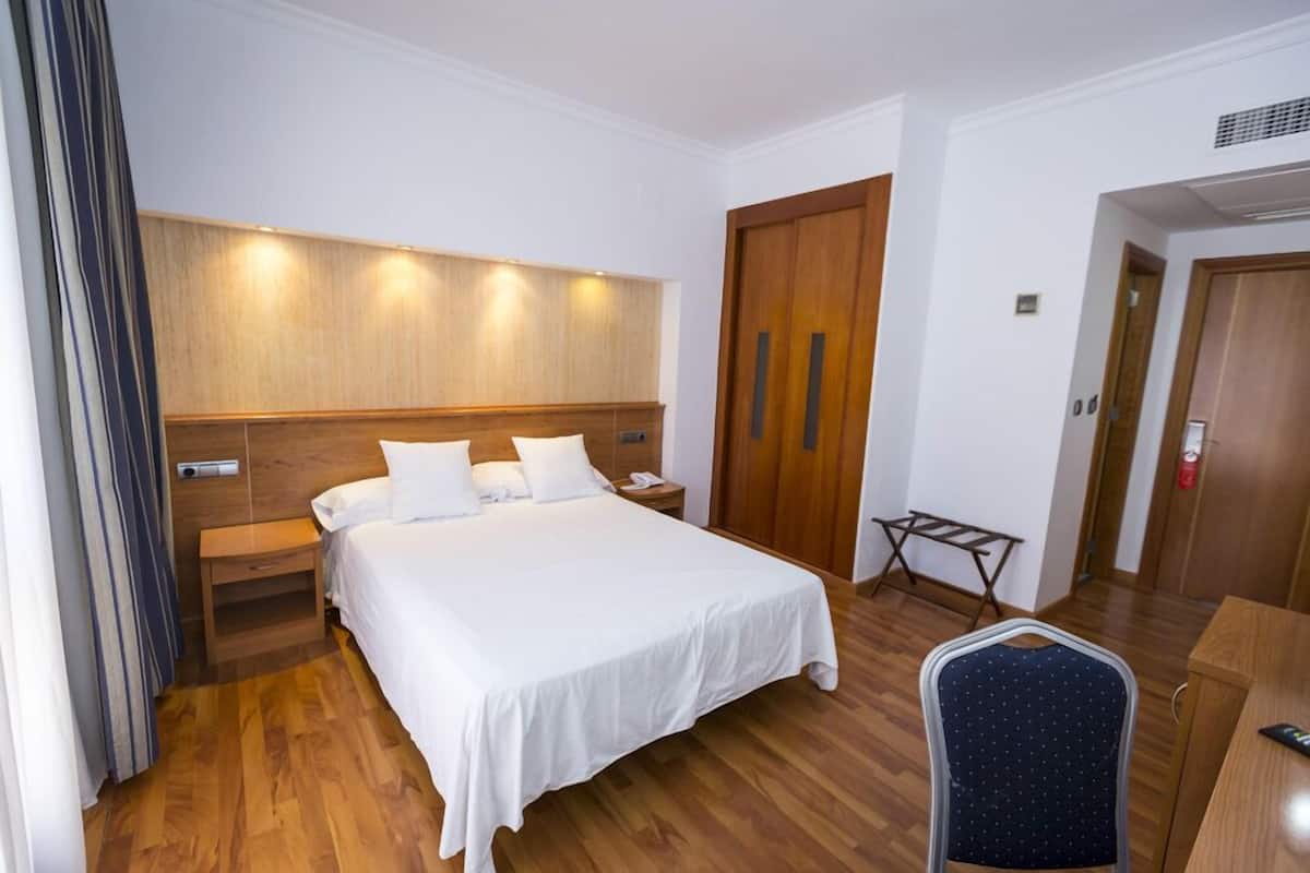 A hotel room with a large bed, wooden headboard, bedside tables, a desk, and a chair.