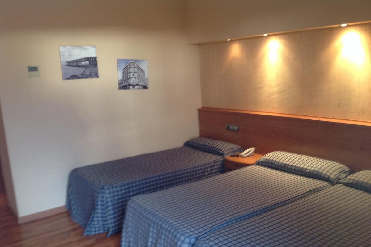A hotel room with two single beds, a wooden headboard, and two framed pictures on the wall.