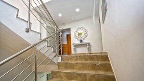 A staircase with a metal railing leading to a landing area with a decorative wall piece and a door. - Hotel Rusadir (Melilla)