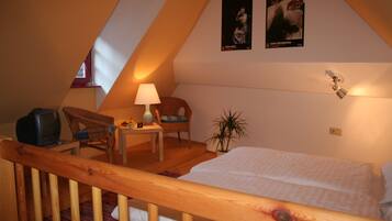 A bedroom with a wooden bed, a desk with a lamp, a chair, and a television.