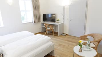Habitación de hotel con cama, escritorio con televisor, silla, mesita con un florero y una botella, y una puerta.