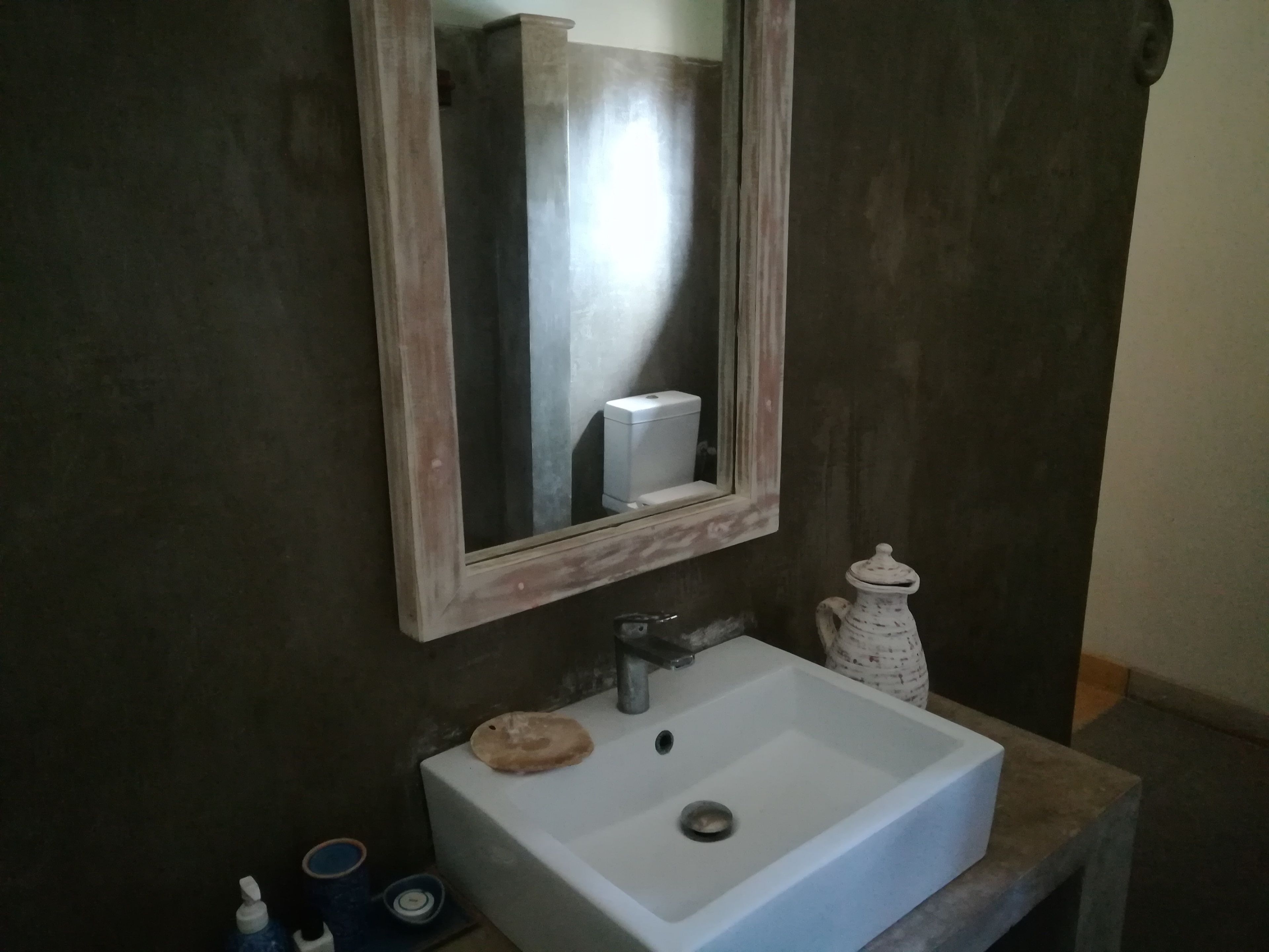 A bathroom with a white sink, a mirror, and a white pitcher.