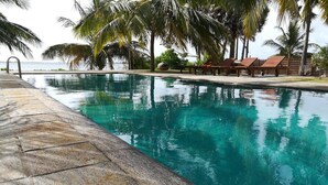 A swimming pool with clear water, surrounded by palm trees and wooden lounge chairs. - Villa Setha Wadi (Kalpitiya)