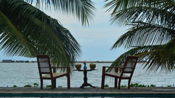 A poolside area with two wooden chairs and a table with drinks, overlooking a body of water. - Villa Setha Wadi (Kalpitiya)