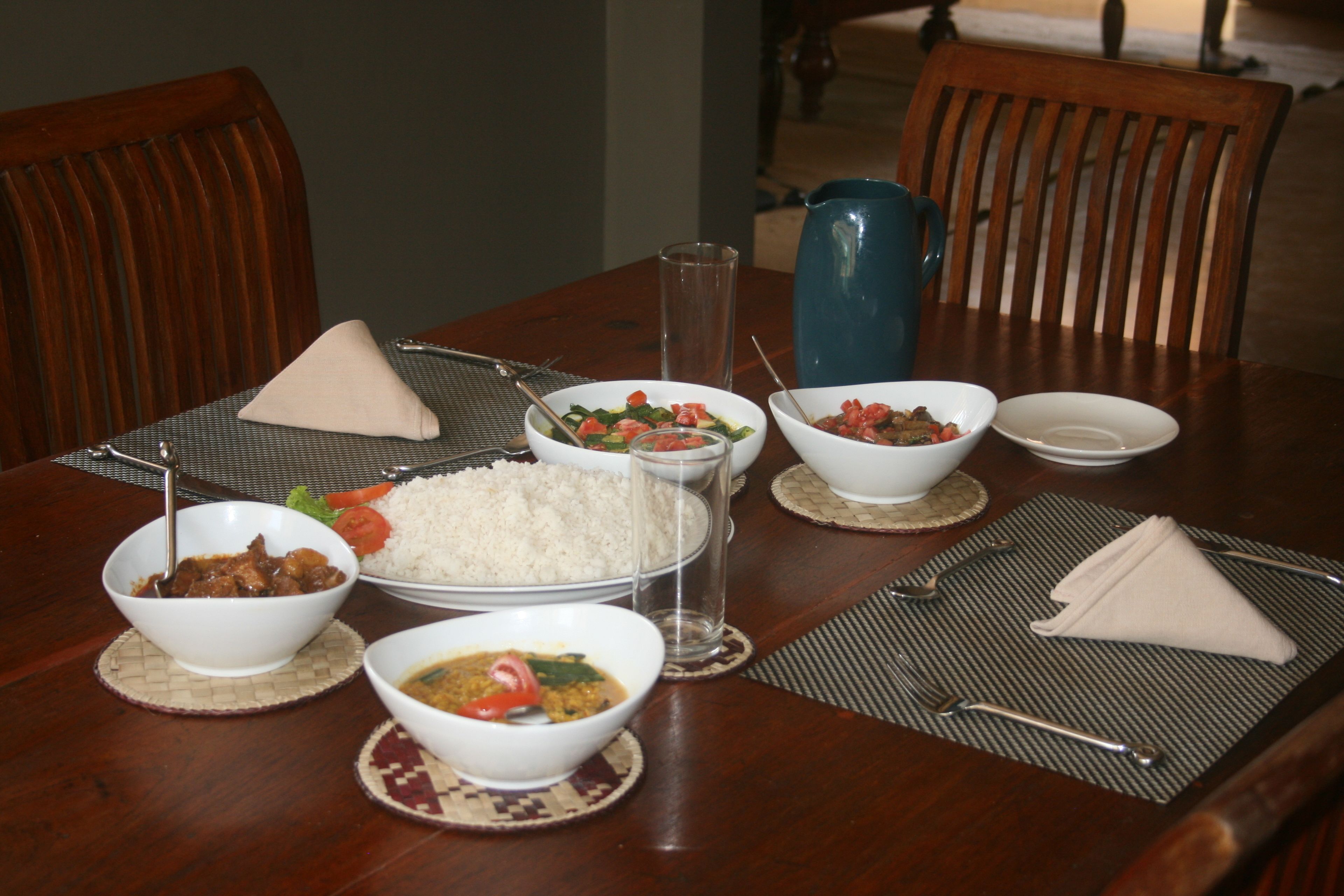 Een eettafel gedekt met diverse gerechten, waaronder rijst, curry en groenten.