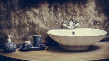 A bathroom with a white sink, a soap dispenser, and a decorative vase on a wooden surface.