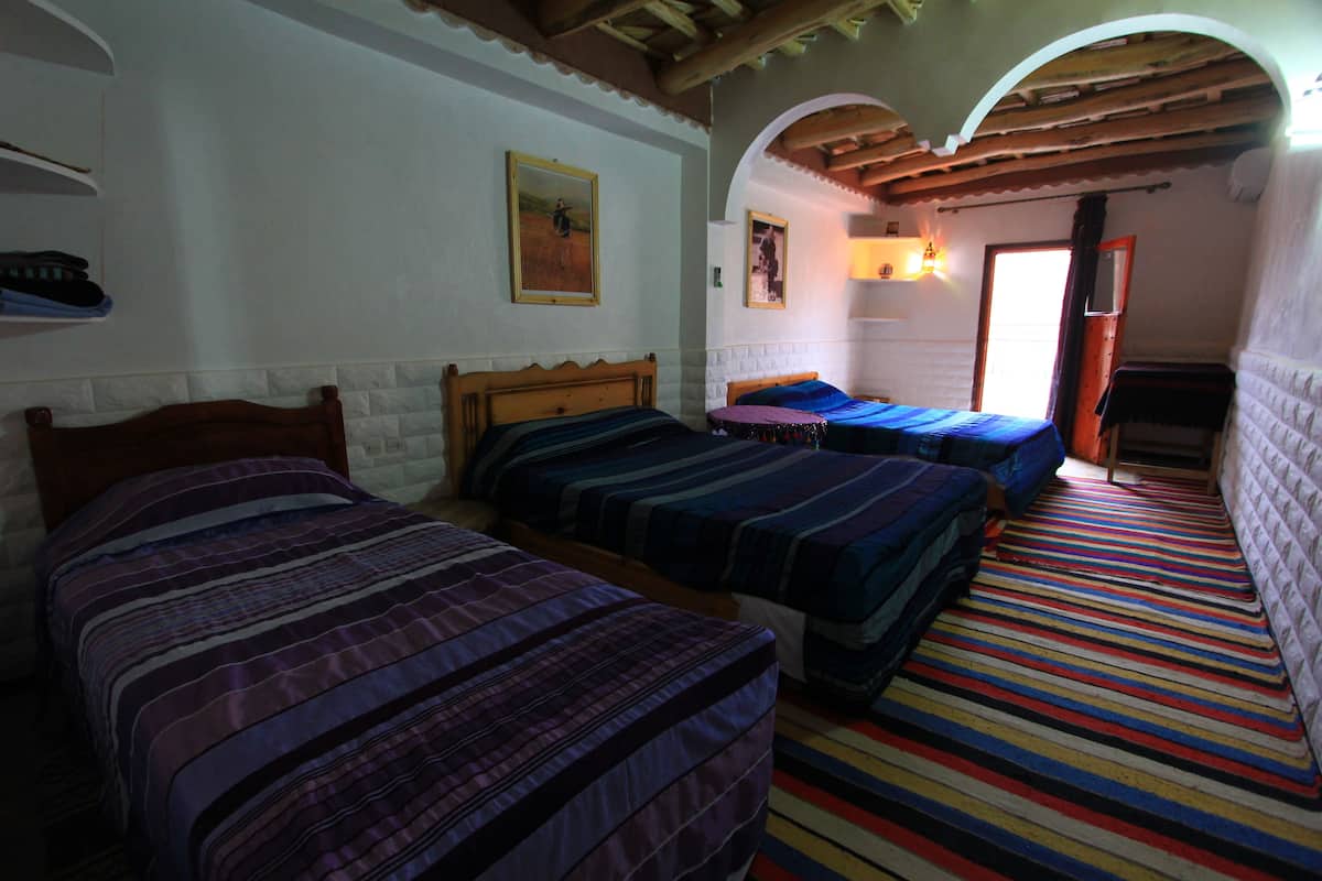 Quarto com três camas, um tapete colorido listrado e teto de madeira.
