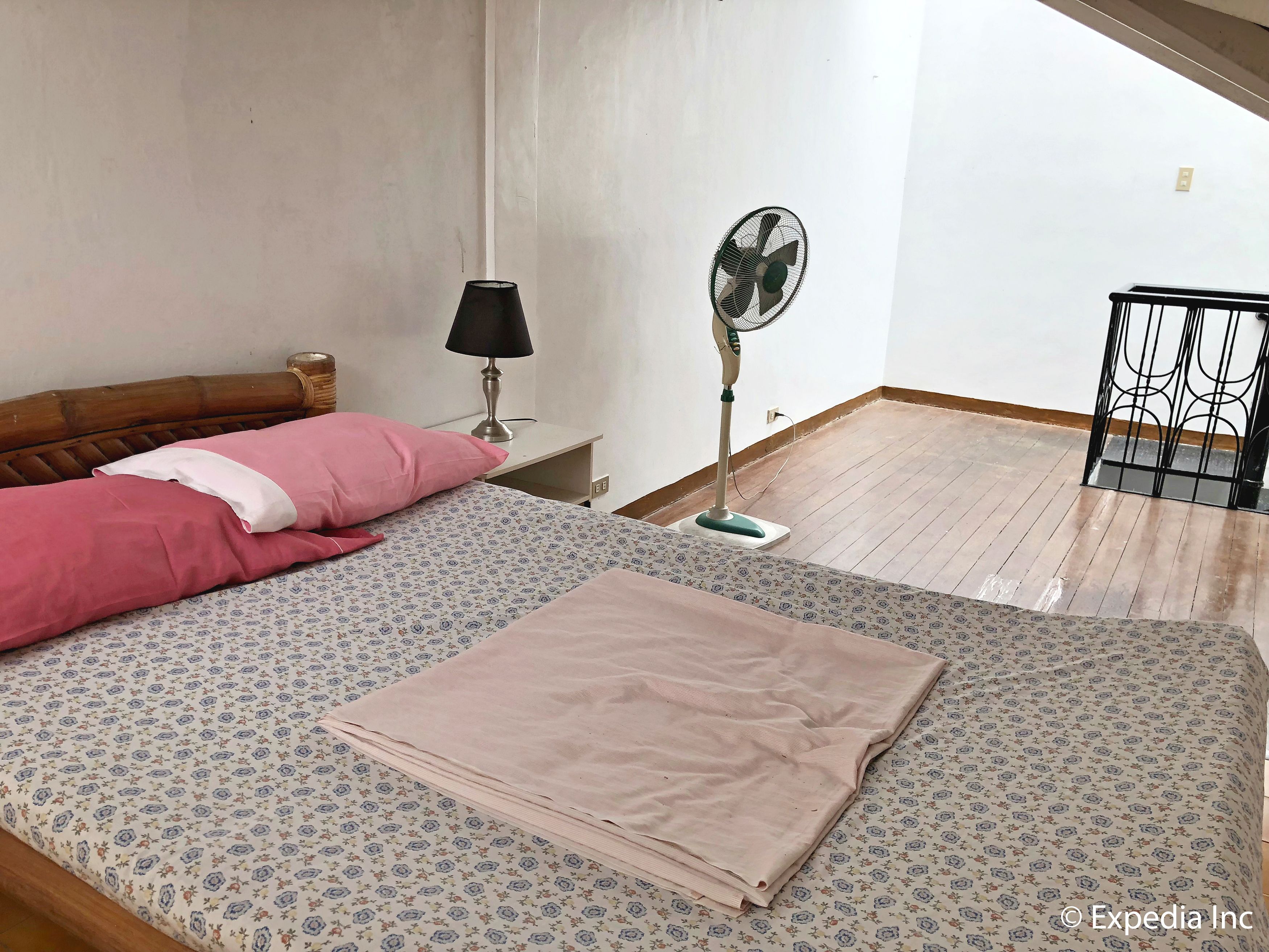 A bedroom with a bed, a standing fan, a nightstand, and a window.