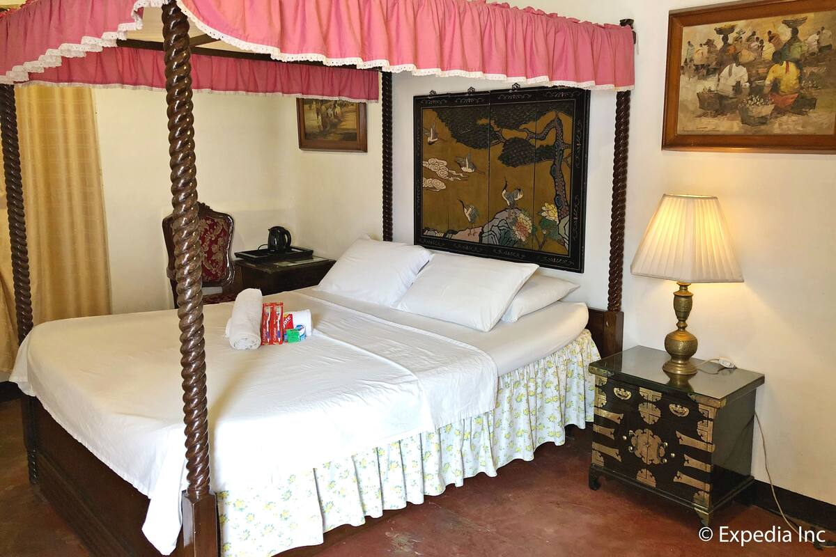 A four-poster bed with a canopy, a nightstand with a lamp, and a painting on the wall.