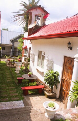 A courtyard with a red-roofed building, outdoor seating, and potted plants. - Casa de Carlo (Tagaytay)