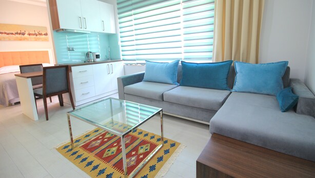 A modern living room with a sofa, a glass coffee table, and a kitchen area with cabinets and a kettle.