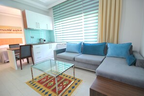Uma sala de estar moderna com sofá, mesa de centro de vidro e área de cozinha com armários e chaleira.