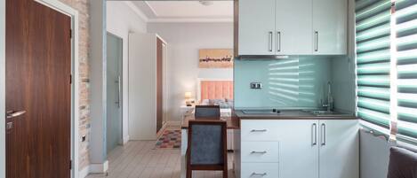 A compact kitchen with white cabinets, a built-in stove, and a window with blinds.