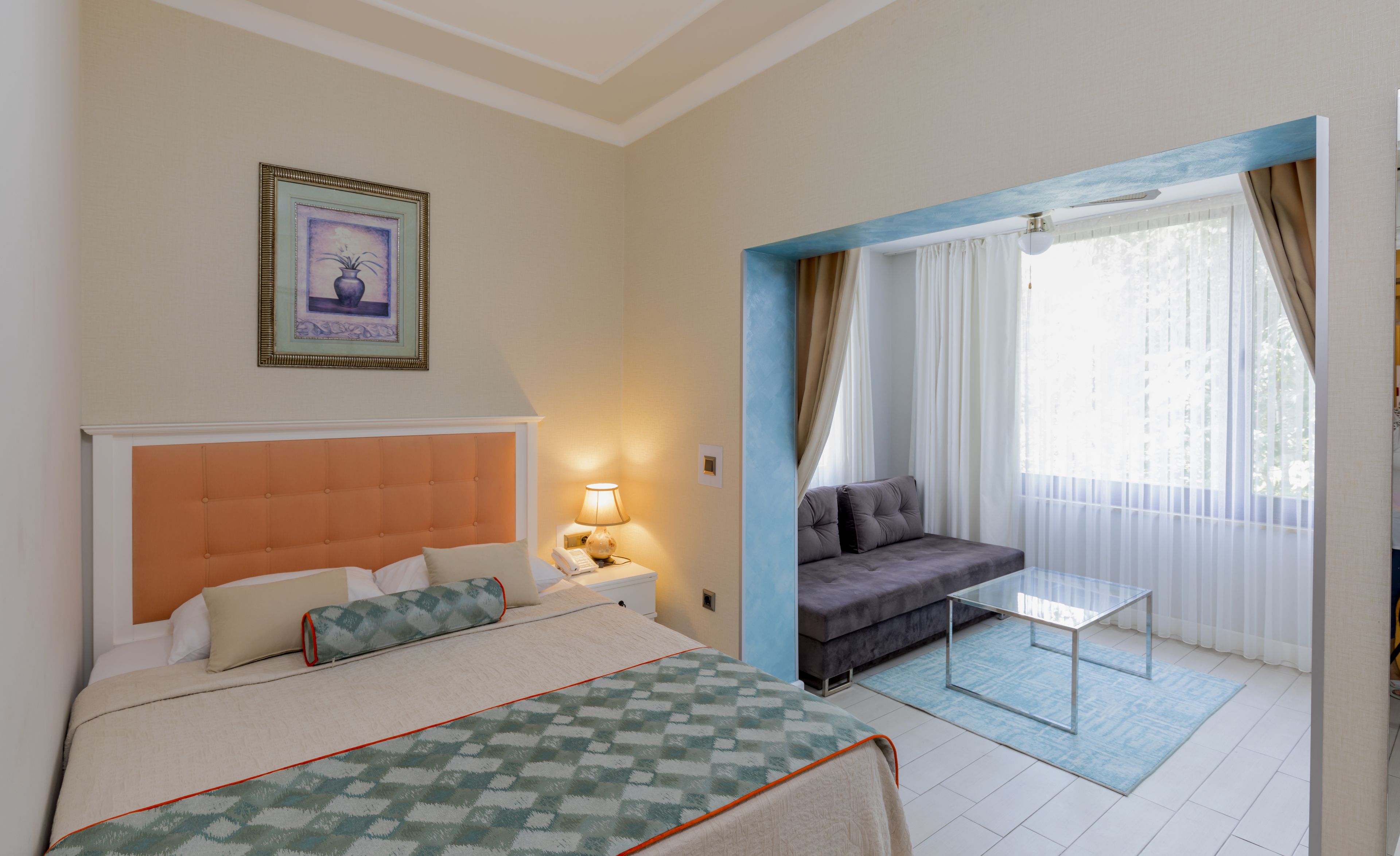 A hotel room with a bed, a sofa, a glass table, and a window with curtains.