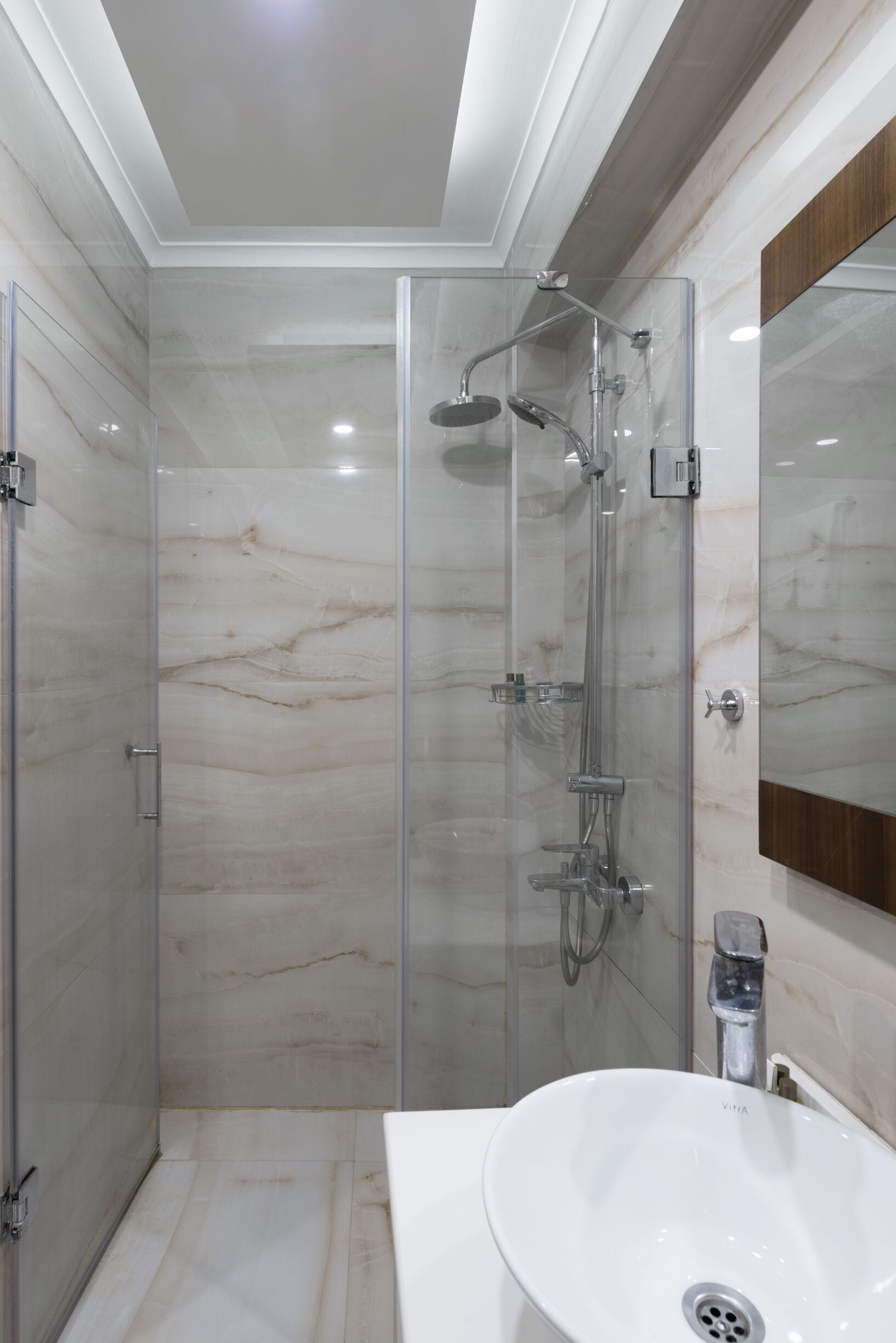 A modern bathroom with a glass-enclosed shower, a white sink, and a wooden vanity.