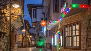 A narrow street with buildings on either side, a theater with colorful lights, and stone walls.