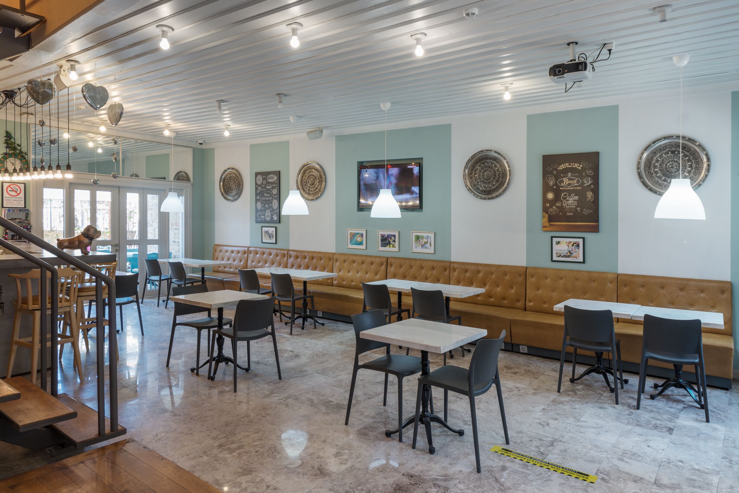 A restaurant with a mix of booths and tables, a staircase, and a ceiling with exposed beams and pendant lights.