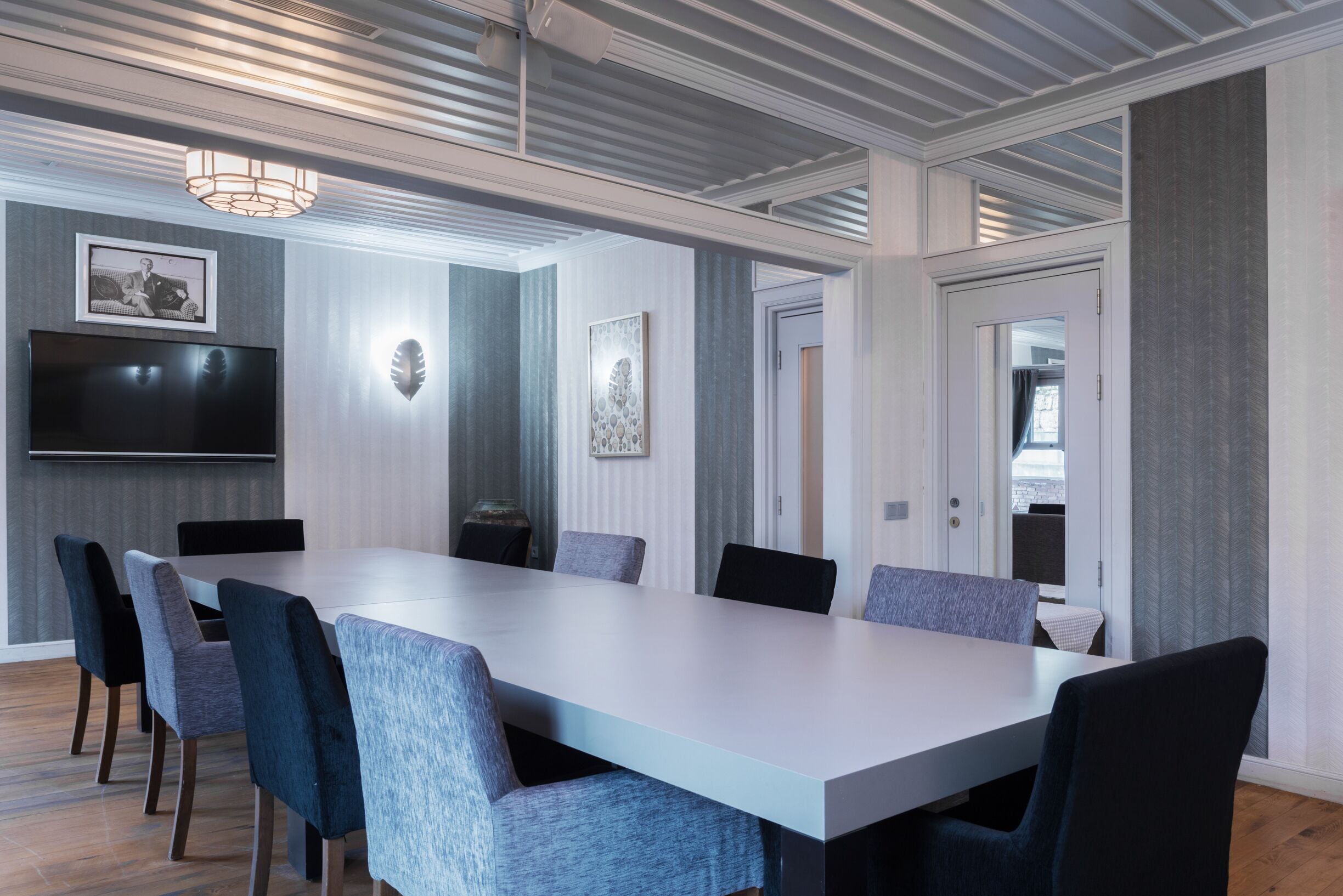 A conference room with a long table, chairs, a flat-screen TV, and framed artwork on the walls.
