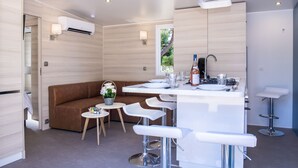 A modern kitchen with a central island, bar stools, a brown sofa, and a small table with a vase of flowers. - Les Mûriers (Vendres)