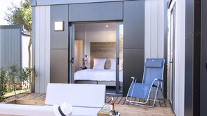 A modern, compact bedroom with a bed, a small seating area, and a wooden deck. - Les Mûriers (Vendres)