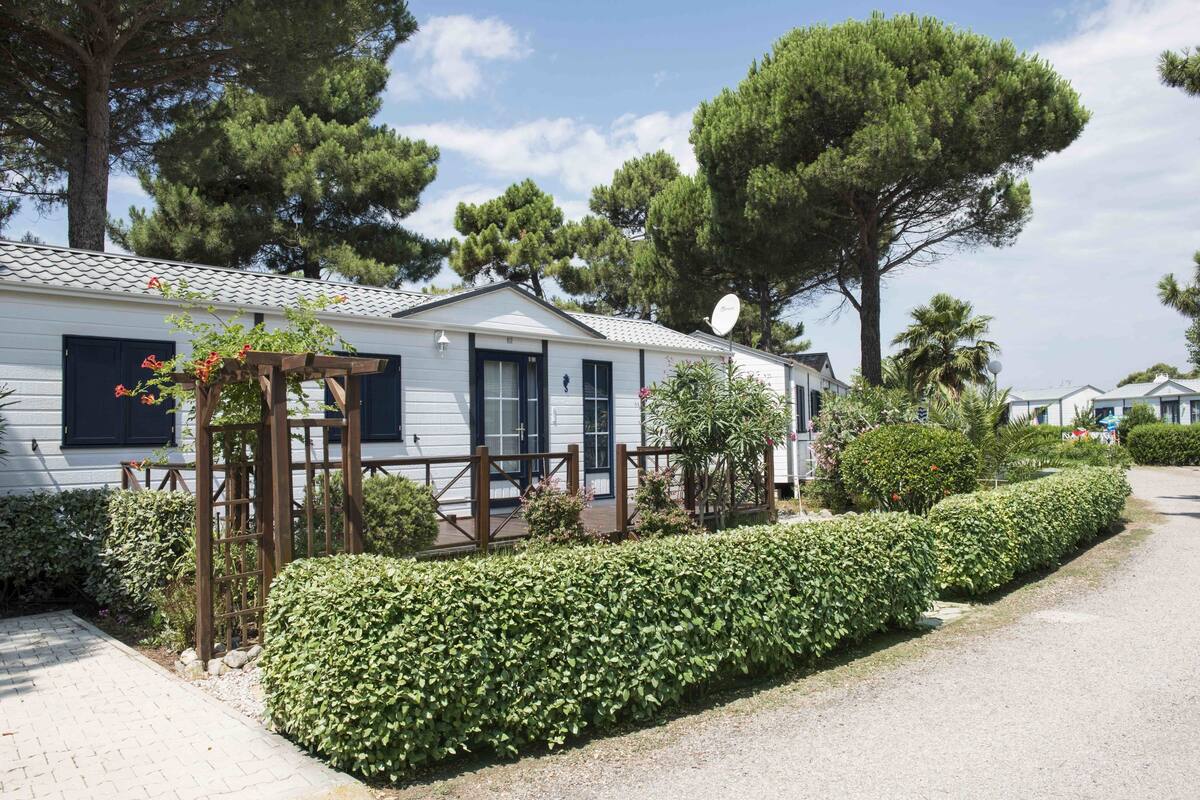 Ein Mobilheim mit Satellitenschüssel, einer Holzpergola mit Blumen und einer gepflegten Hecke.