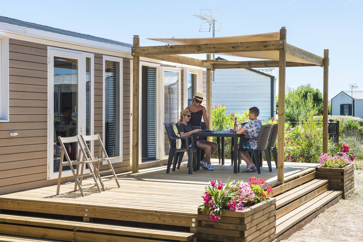 Eine Holzterrasse mit Tisch und Stühlen, umgeben von Kübeln mit Blumen.