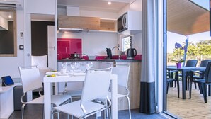 A modern kitchen with white cabinets, a microwave, and a coffee maker. There is a dining area with white chairs and a table set for two. - Les Mûriers (Vendres)