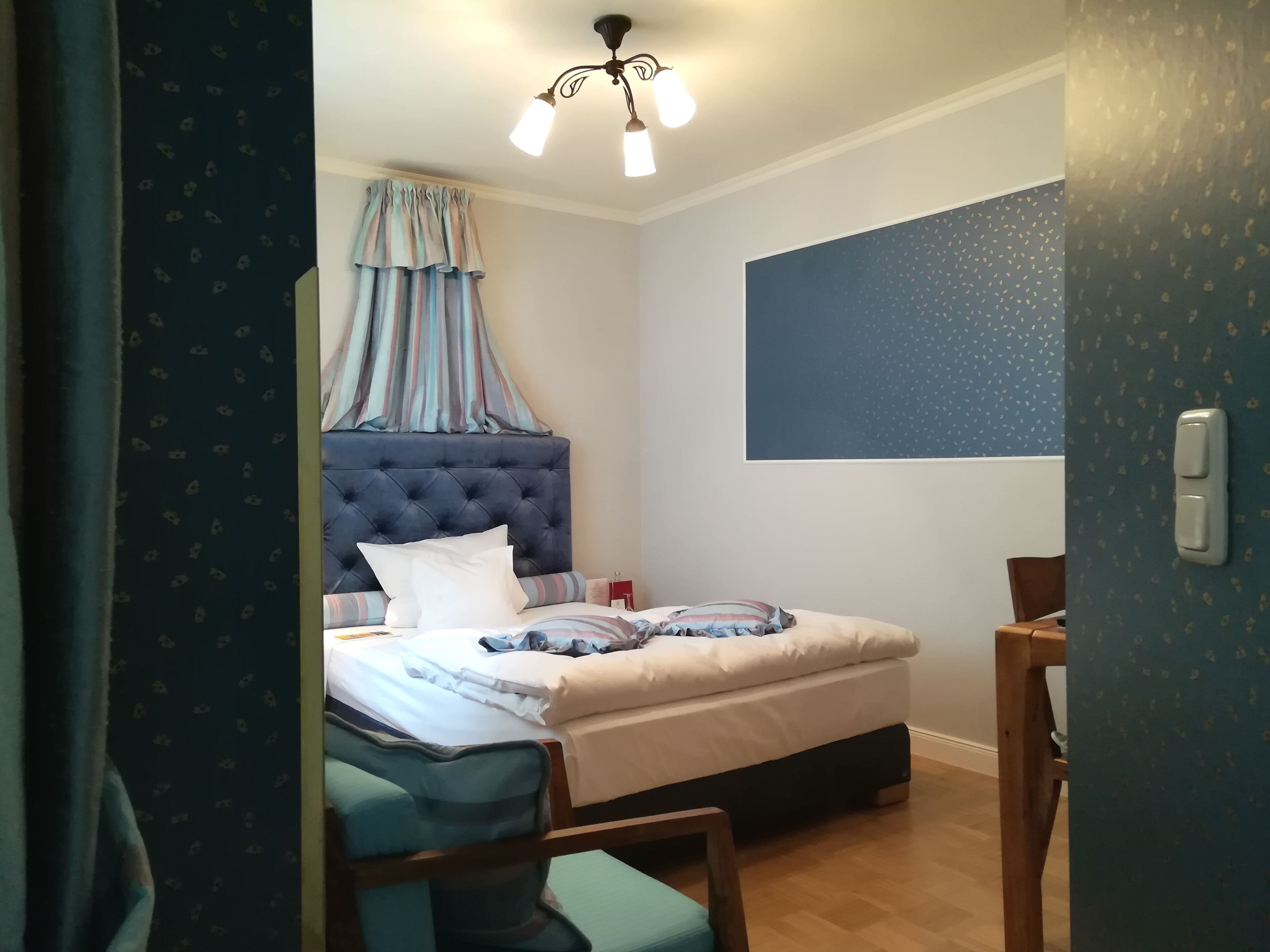 A bedroom with a tufted headboard, a bed with striped bedding, a bedside table, a chair, and a ceiling light fixture.