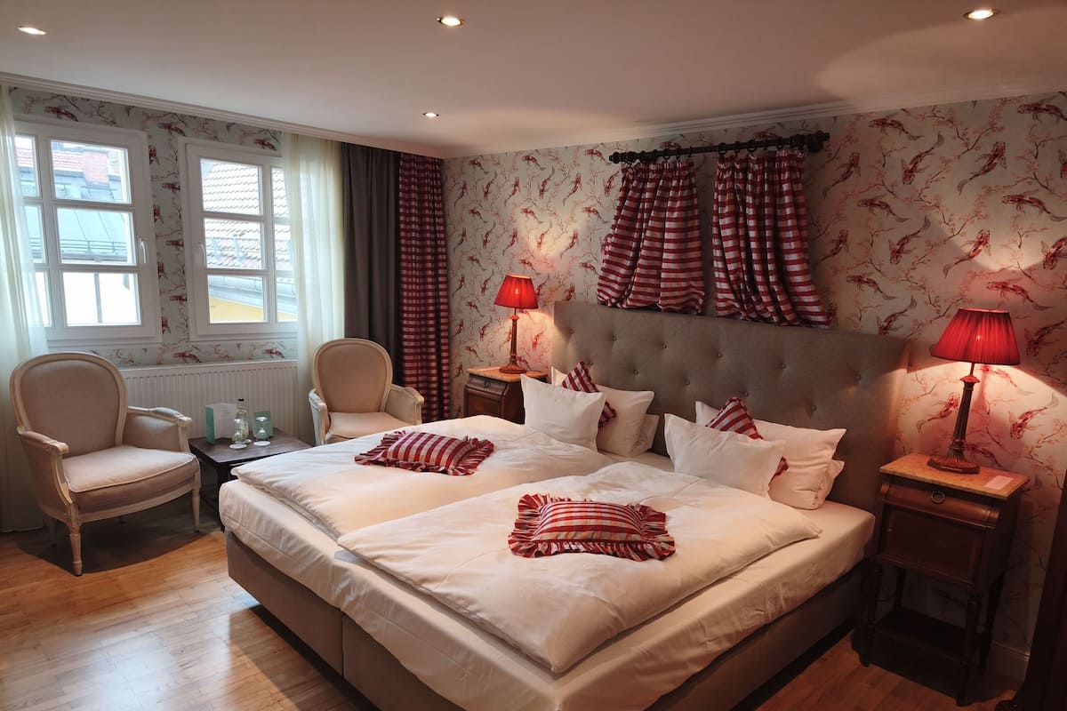 A bedroom with two beds, a chair, a nightstand, and a window with curtains.