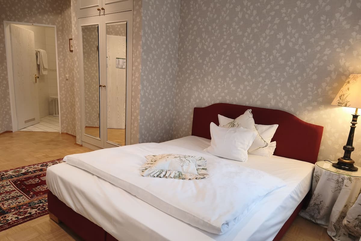 A neatly made bed with white linens and decorative pillows, a red headboard, and a bedside lamp.