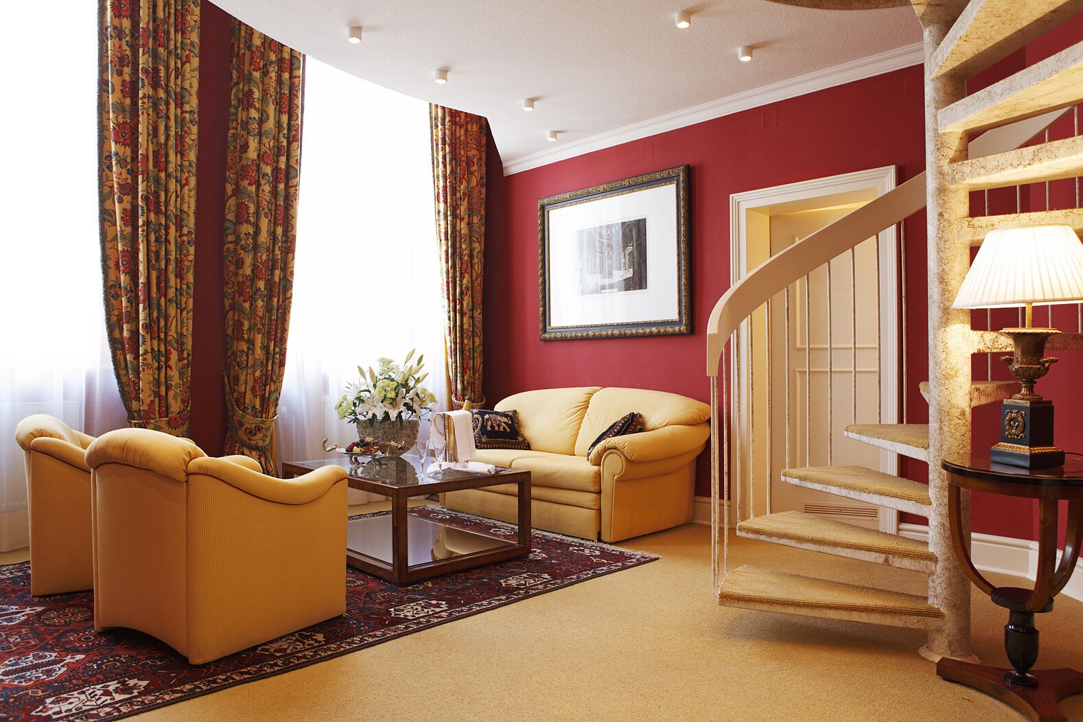 A living room with a yellow sofa, a coffee table, and a staircase with a lamp.