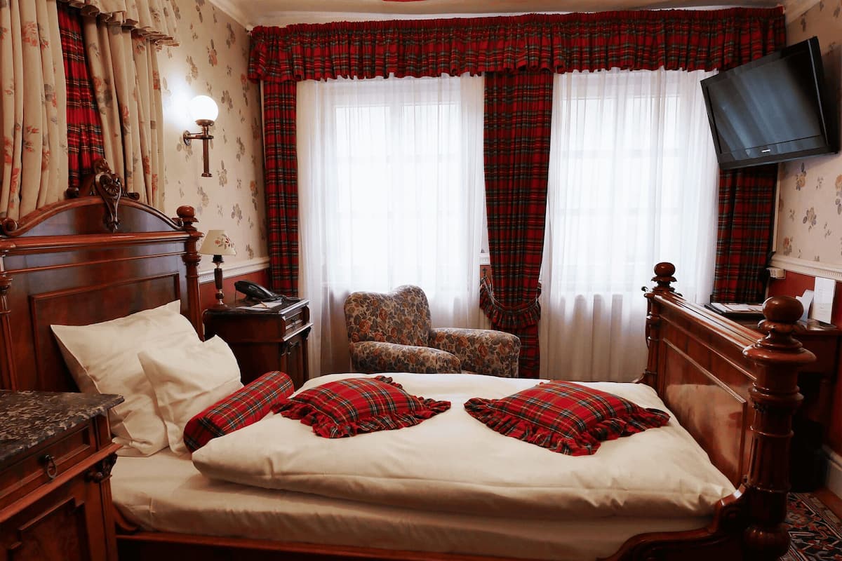 A hotel room with a wooden bed, a chair, a desk with a telephone, and a television mounted on the wall.